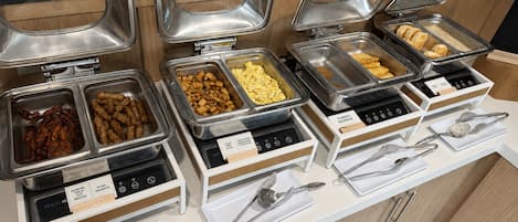 Buffet com diversas opções de comida, incluindo bacon, linguiça, ovos e batatas.