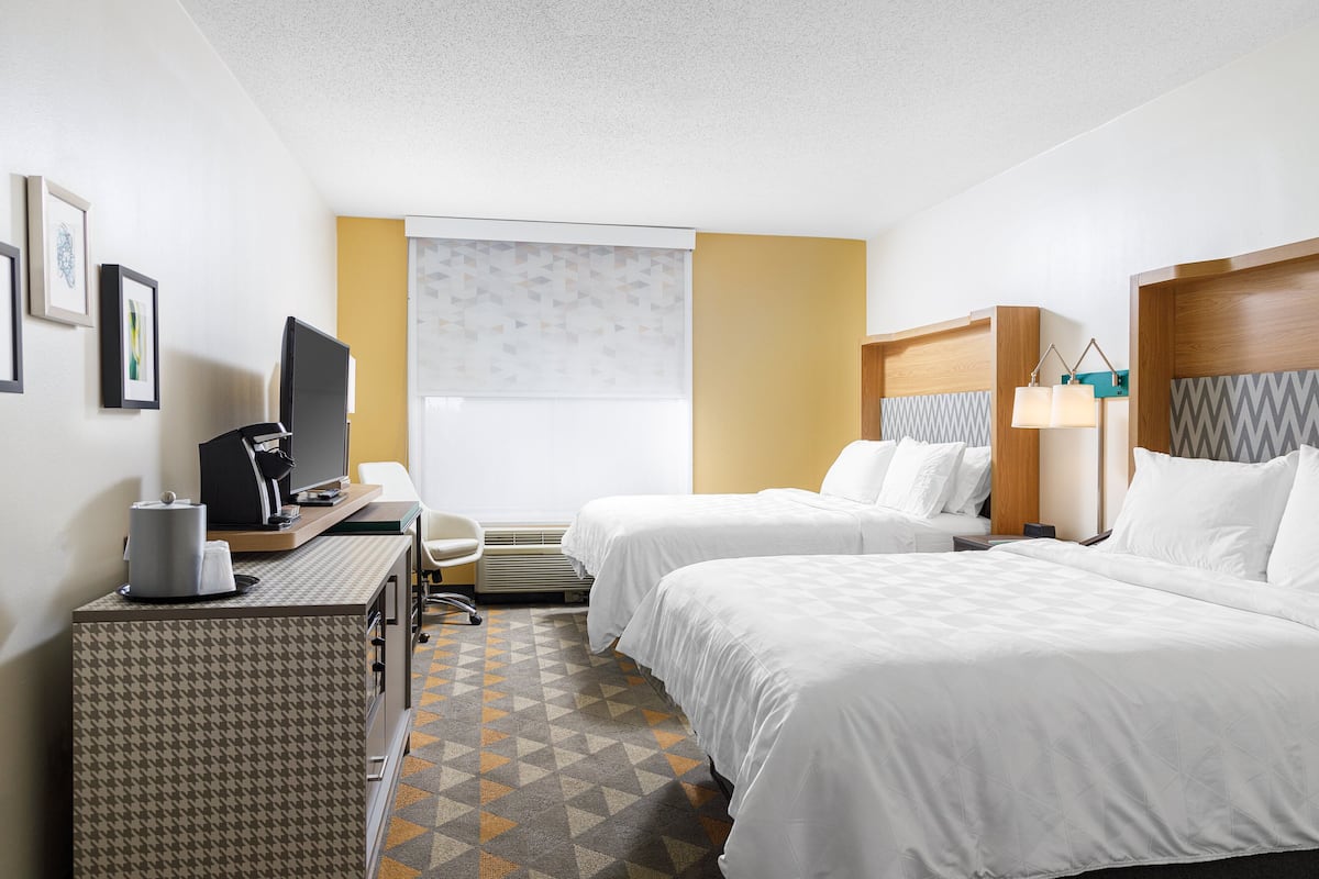 Habitación de hotel con dos camas, un escritorio con computadora, una silla y una ventana con persianas.