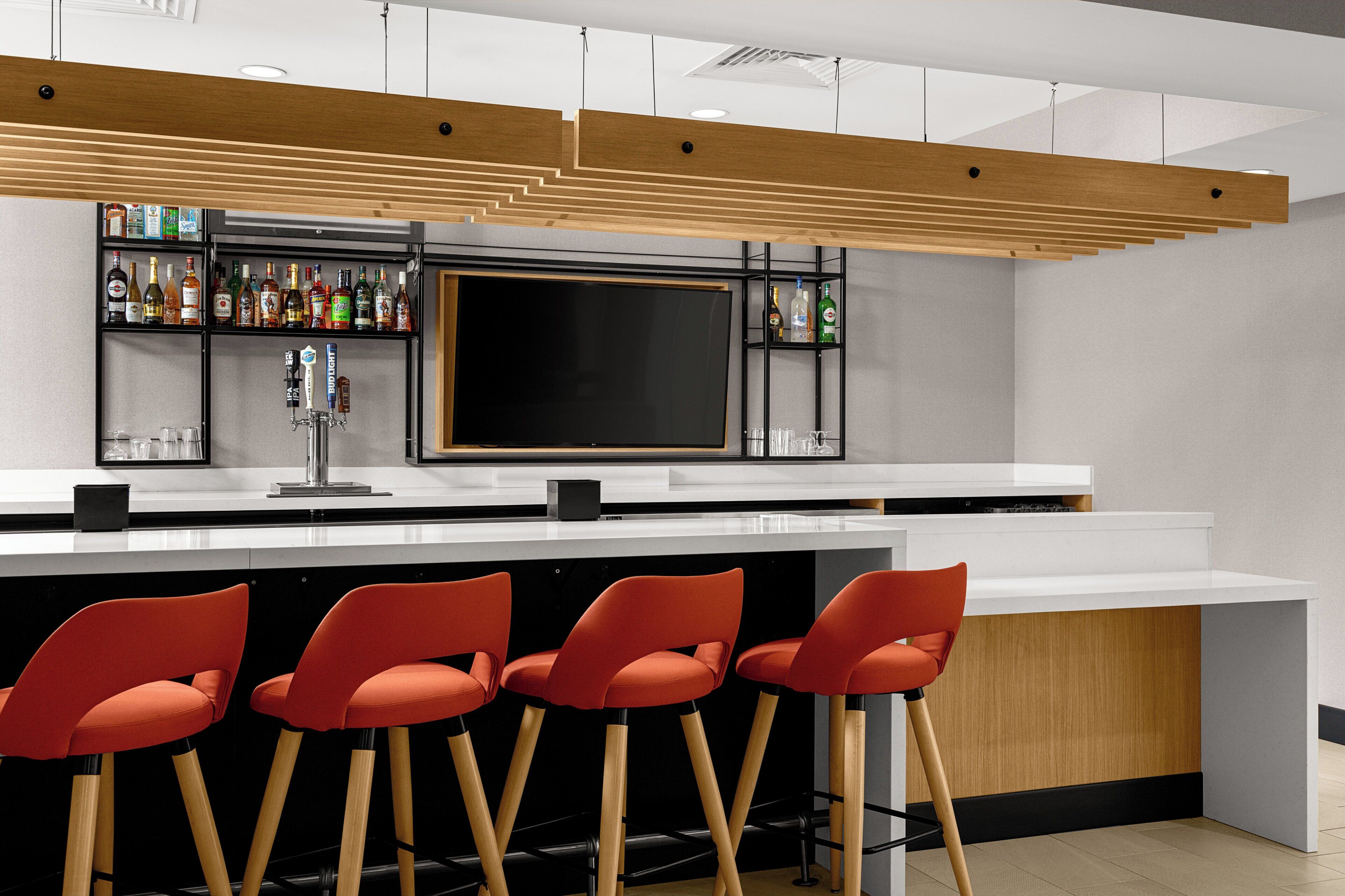 A bar area with a flat-screen TV, multiple liquor bottles, and red bar stools.
