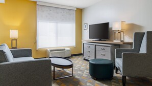 A hotel room with a sofa, a small table, a TV, a cabinet, and a window with blinds. - Holiday Inn Cleveland by IHG (Cleveland)