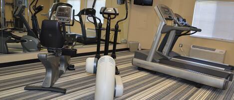 A gym with cardio machines, a mirrored wall, and a television.