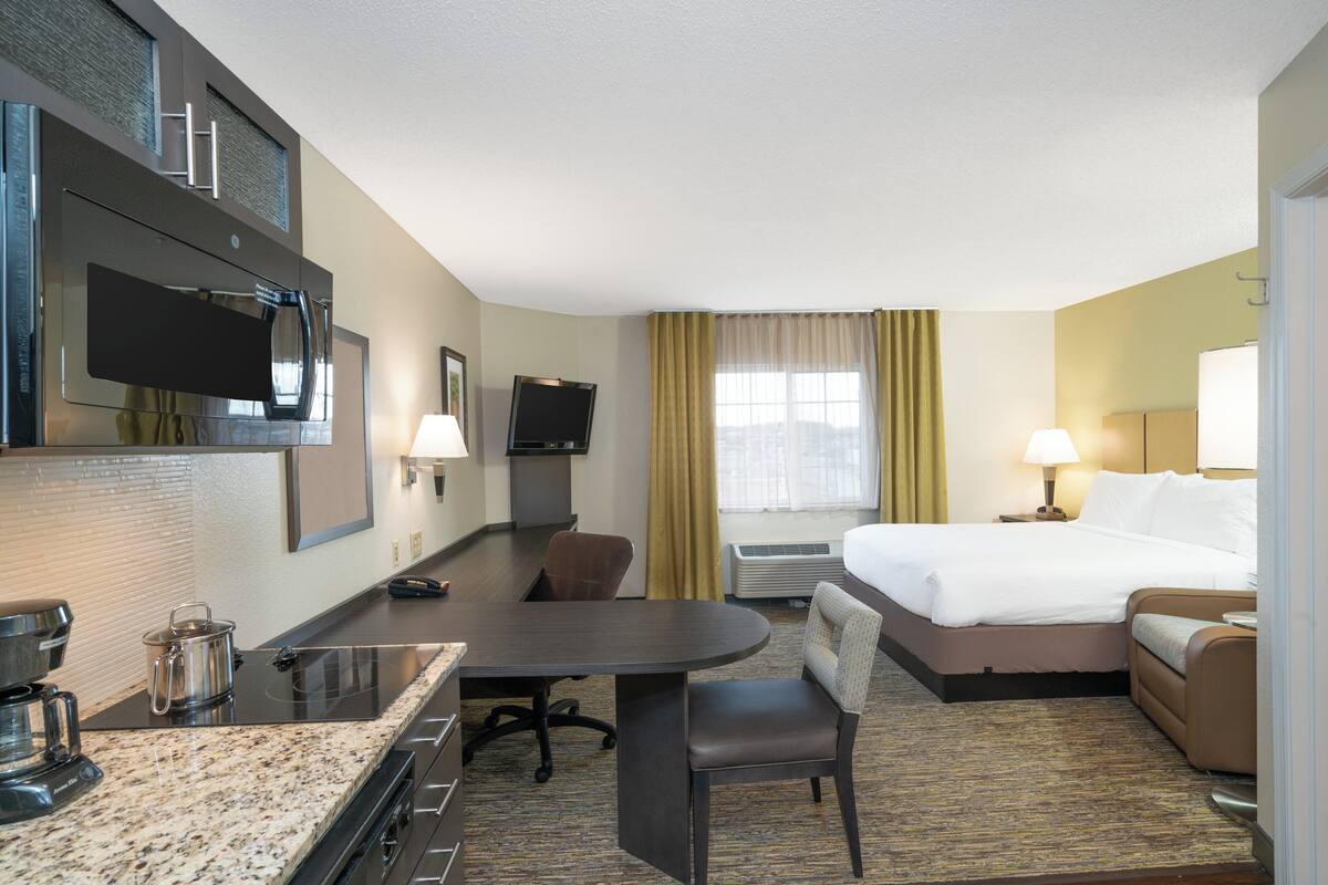 Una habitación de hotel con cama, escritorio, silla, televisor y cafetera.
