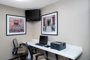Um espaço de trabalho com escrivaninha, duas cadeiras, um laptop, uma impressora e duas molduras na parede.
