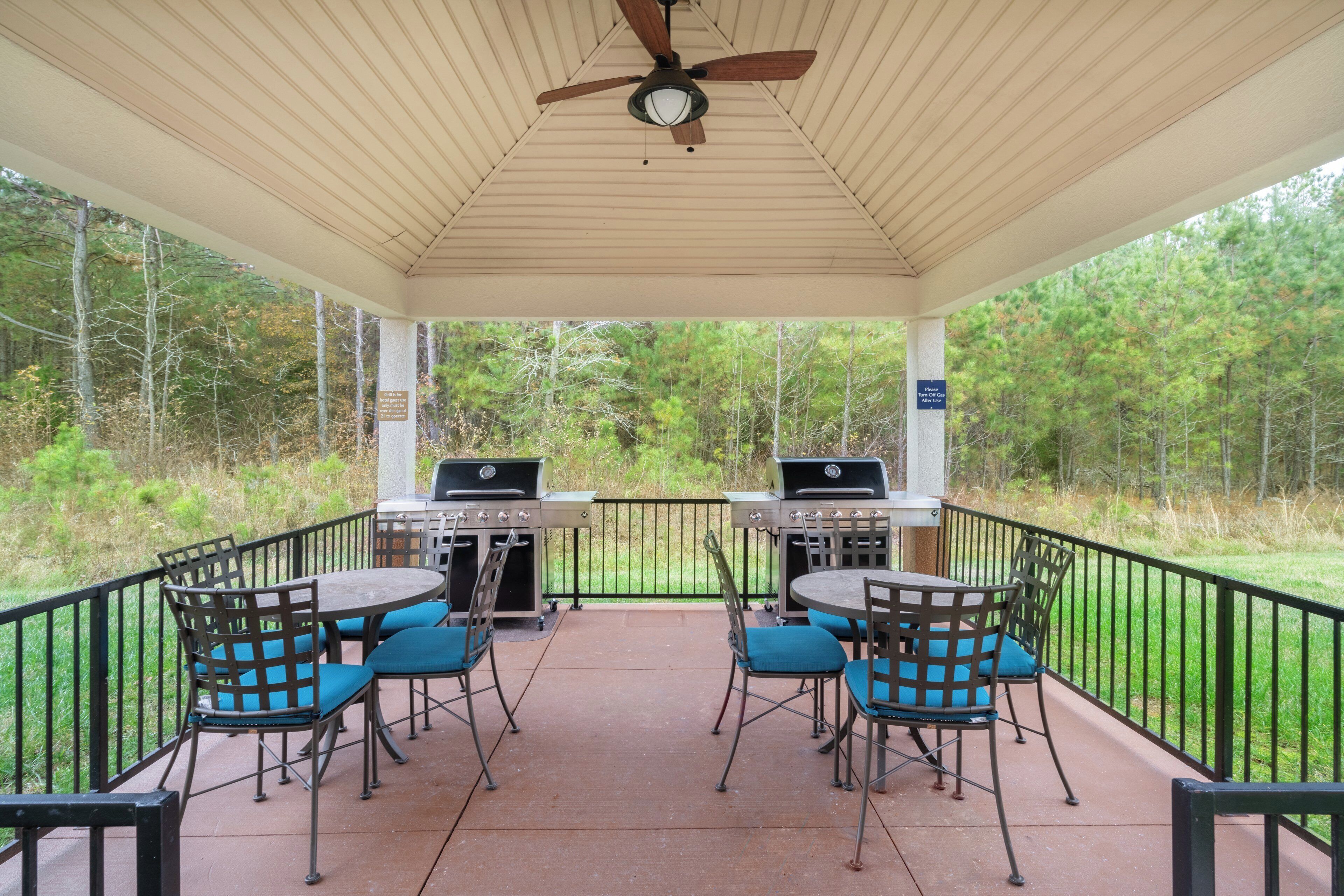 A covered patio with two barbecue grills, outdoor seating with chairs, and a ceiling fan.