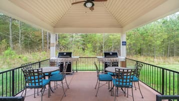 A covered patio with two barbecue grills, outdoor seating with chairs, and a ceiling fan.
