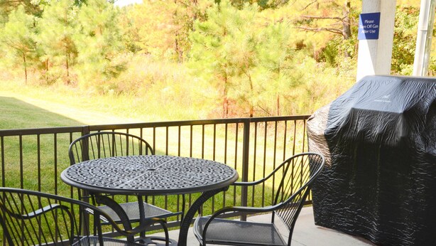 An outdoor patio with a round metal table and chairs, a grill, and a sign instructing to turn off gas after use.