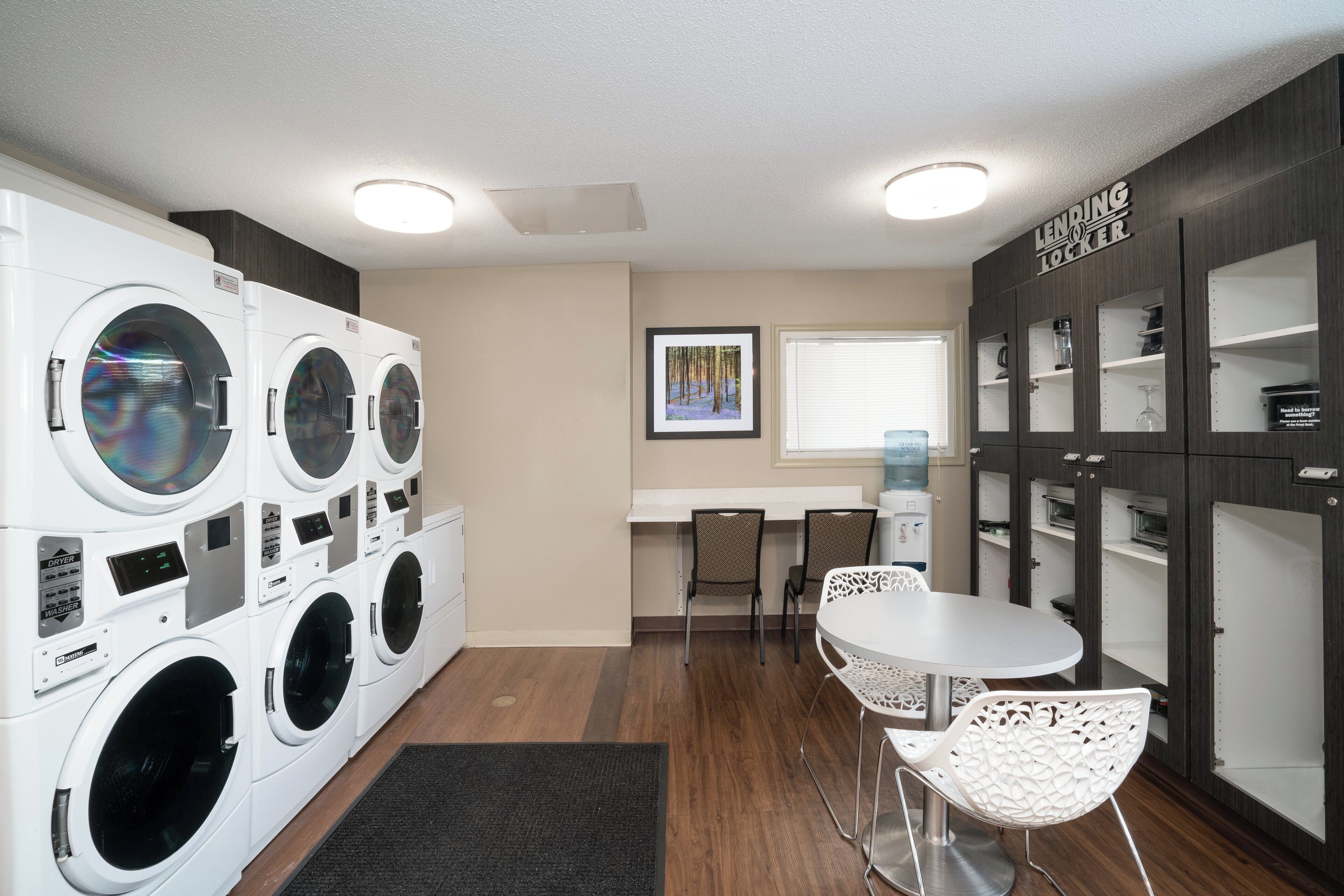 A laundry room with multiple washing machines, a small table with chairs, and a cabinet with storage space.
