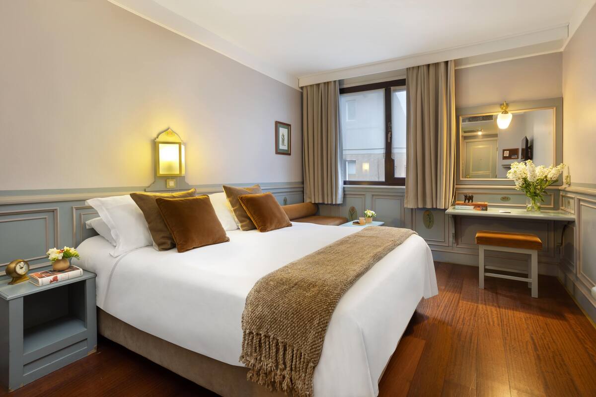 A neatly arranged hotel room with a large bed, bedside table, and a desk with a chair.