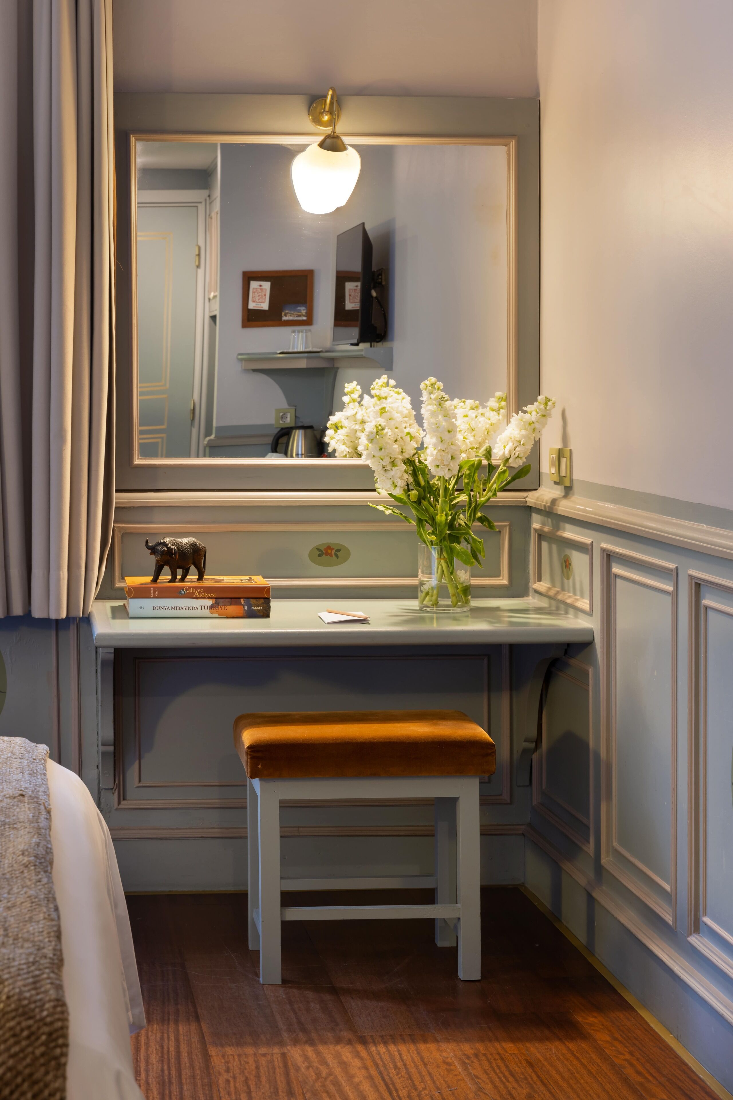 A bathroom with a vanity, a mirror, a bench, and a vase with flowers.