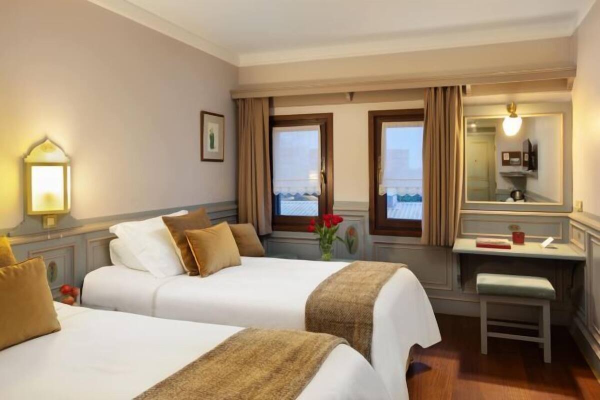 A hotel room with two beds, a desk, a chair, a mirror, and a window with a view.