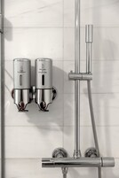 A modern bathroom with a chrome showerhead, a handheld showerhead, and two wall-mounted dispensers for hair conditioner and shower gel.