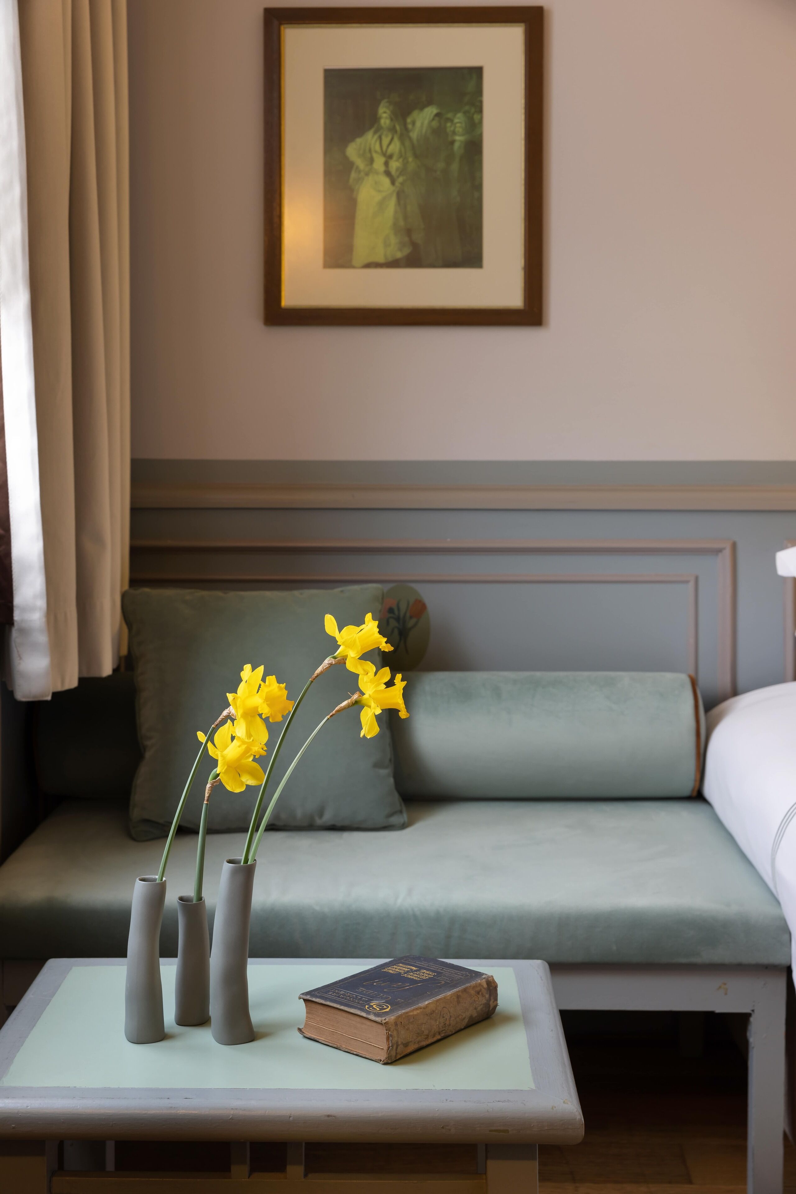 A room with a light green sofa, a small table with three vases and a book, and a framed picture on the wall.