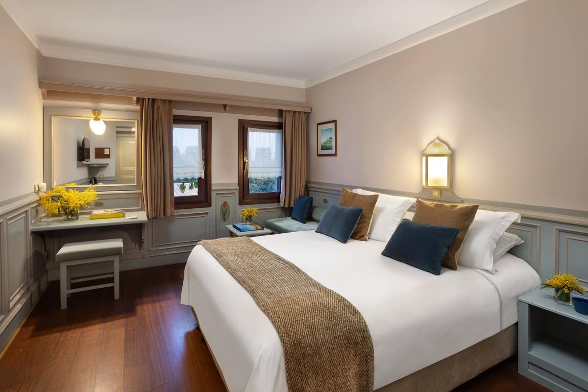 A hotel room with a large bed, a desk with a mirror, and a window with curtains.