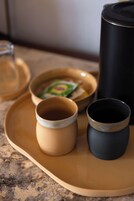 Un vassoio con due tazze in ceramica e un contenitore nero, forse un thermos, su un piano di lavoro in granito.