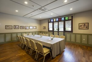 Ein Konferenzraum mit langem Tisch, Stühlen, gerahmten Bildern an den Wänden und Fenstern mit Buntglas.