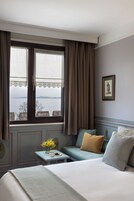 Una camera d'albergo con un letto, un divano, un tavolino con un vaso di fiori e una finestra con tende.
