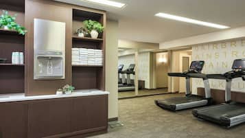 A hotel fitness center with exercise equipment, a water dispenser, and neatly arranged towels.