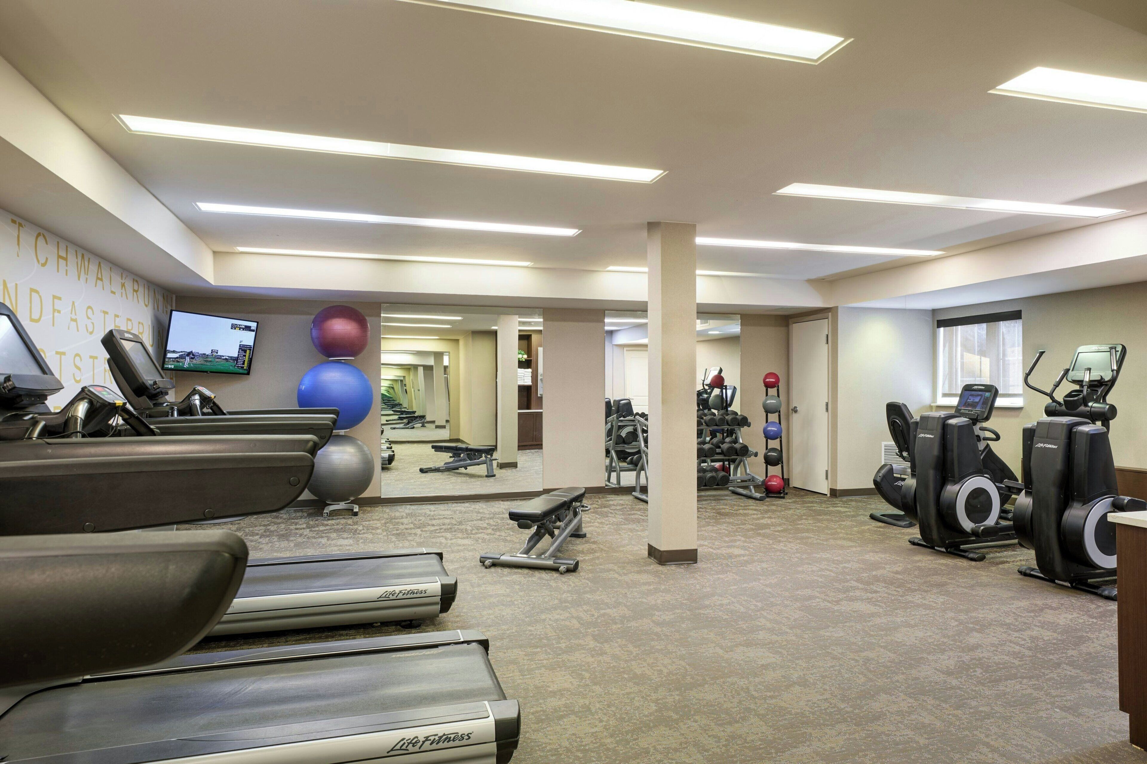 Une salle de sport équipée de tapis de course, de vélos elliptiques et de ballons d’exercice.