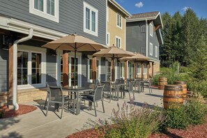 Une terrasse extérieure avec des tables et des chaises, entourée de plantes et de barils.