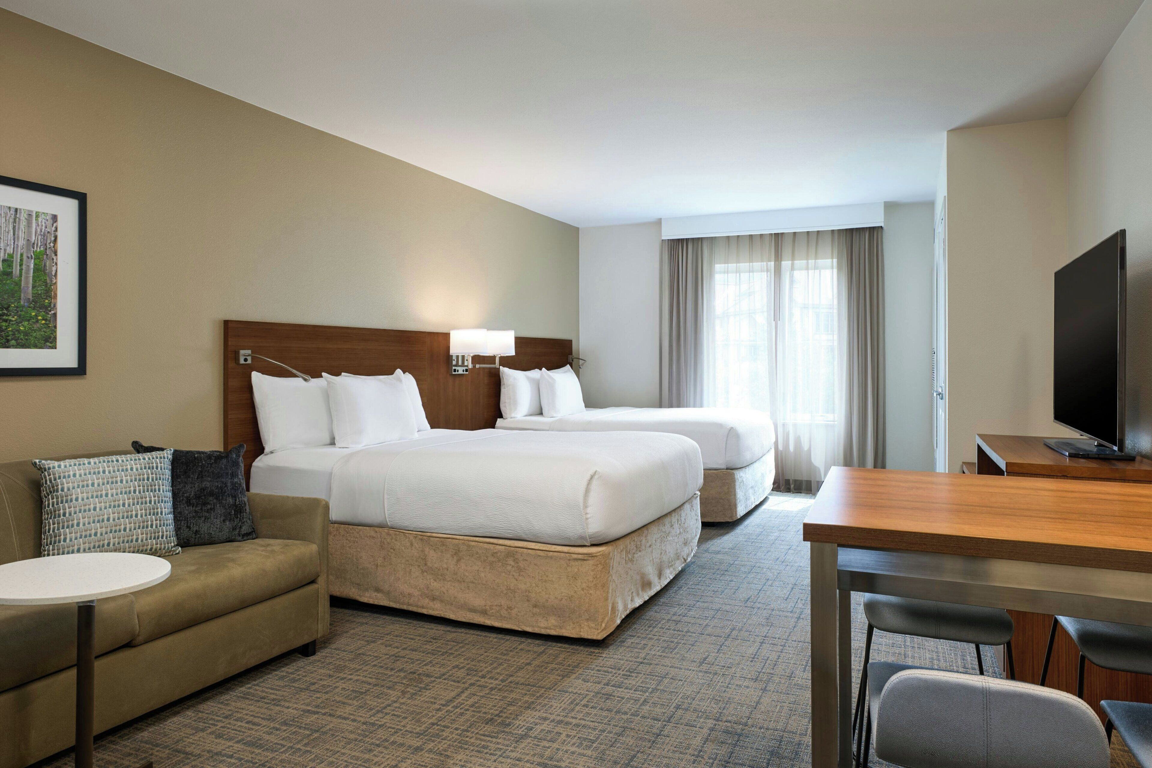 A hotel room with a bed, a sofa, a TV, and a desk.