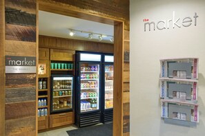 A section of a hotel with wooden paneling, a refrigerated display case with beverages, and a wall with 'The Market' sign and newspapers.