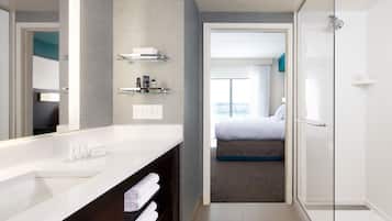 A modern hotel bathroom with a large mirror, white sink, and a glass shower enclosure.
