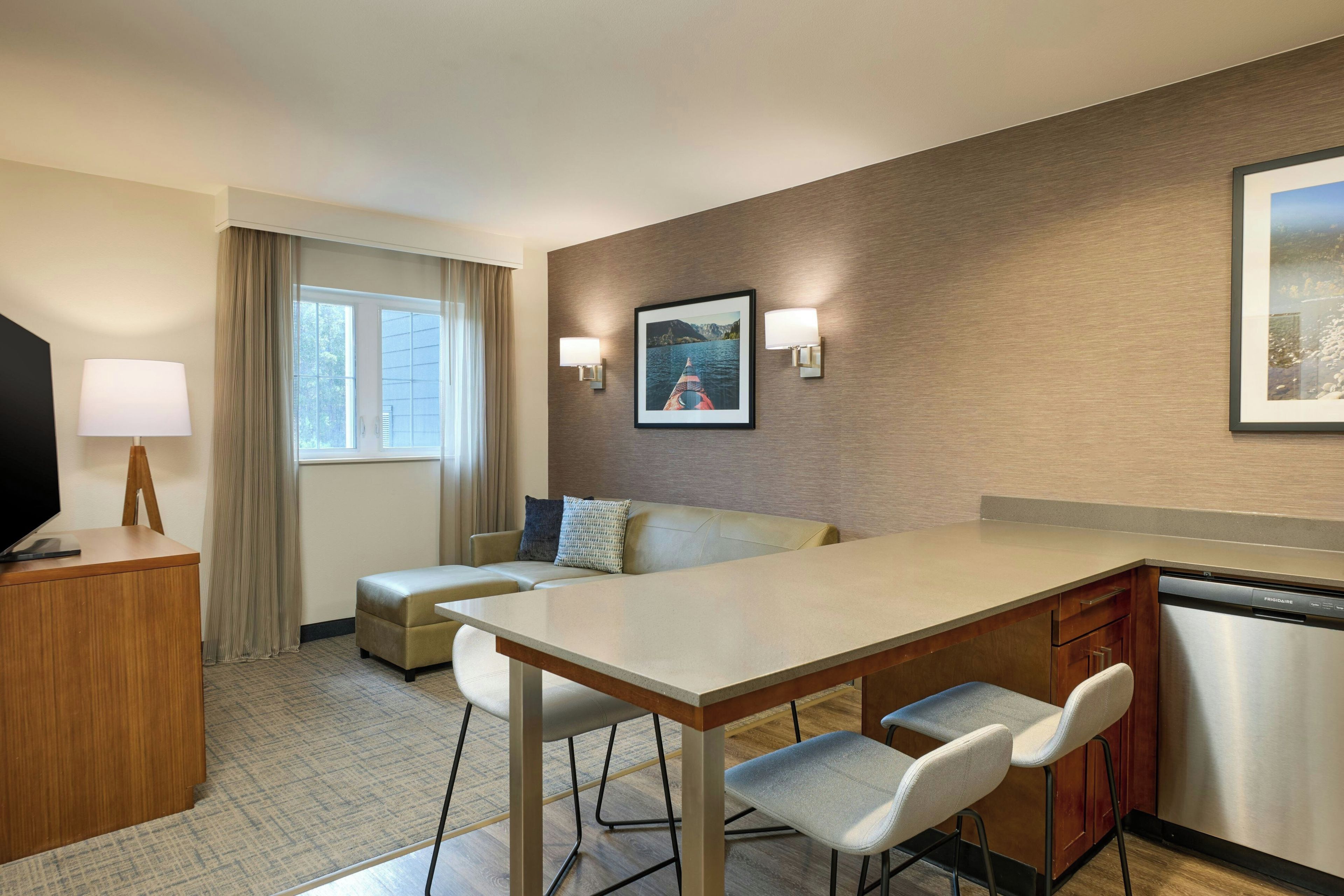 A hotel room with a dining area, a TV, a sofa, and a large window.
