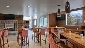 A modern bar area with wooden bar counters, red cushioned bar stools, and a fireplace.