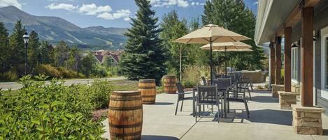 A patio area with outdoor seating, wooden barrels, and a view of mountains.