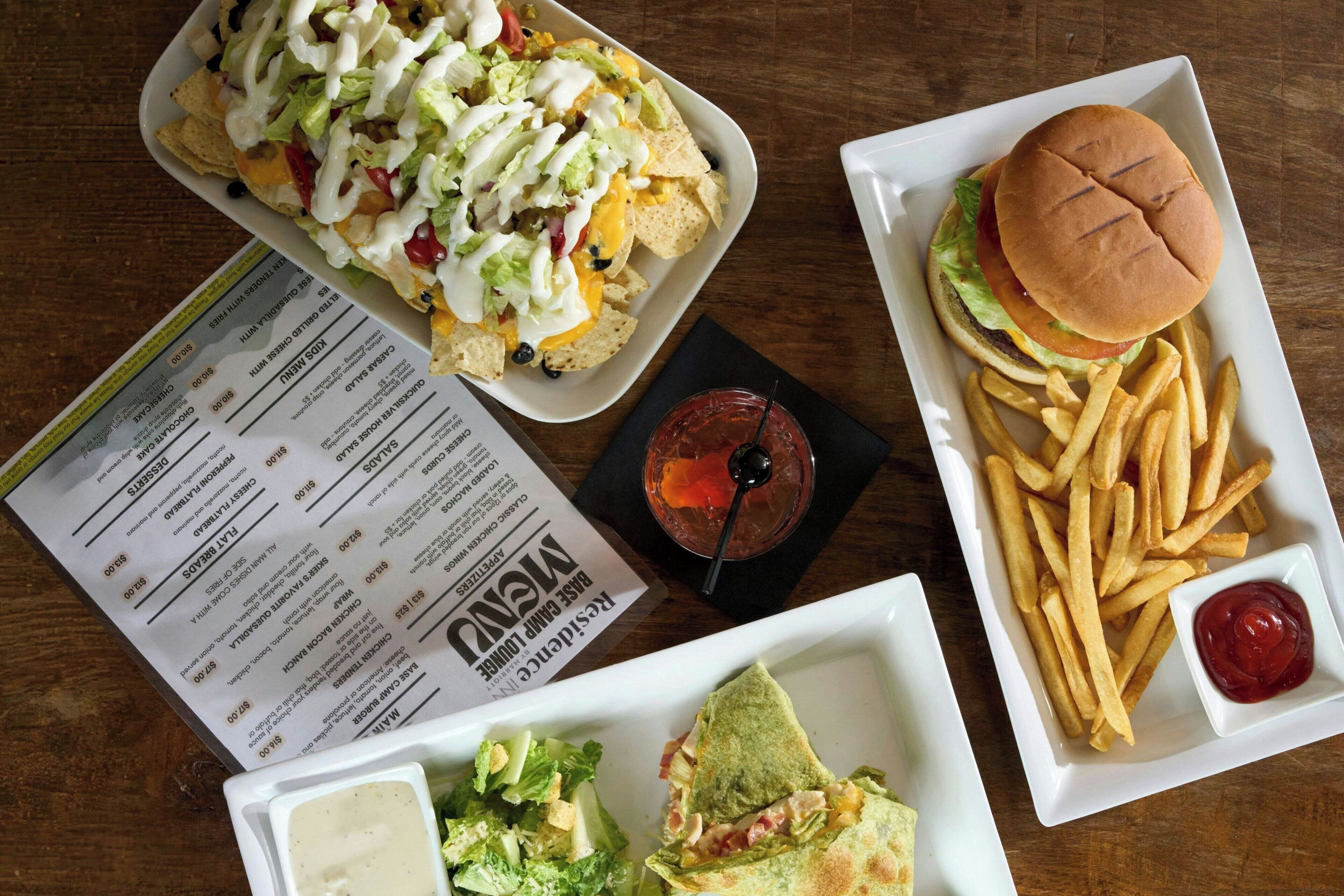 A menu with food items and prices, a plate of nachos, a burger, fries, and a drink.