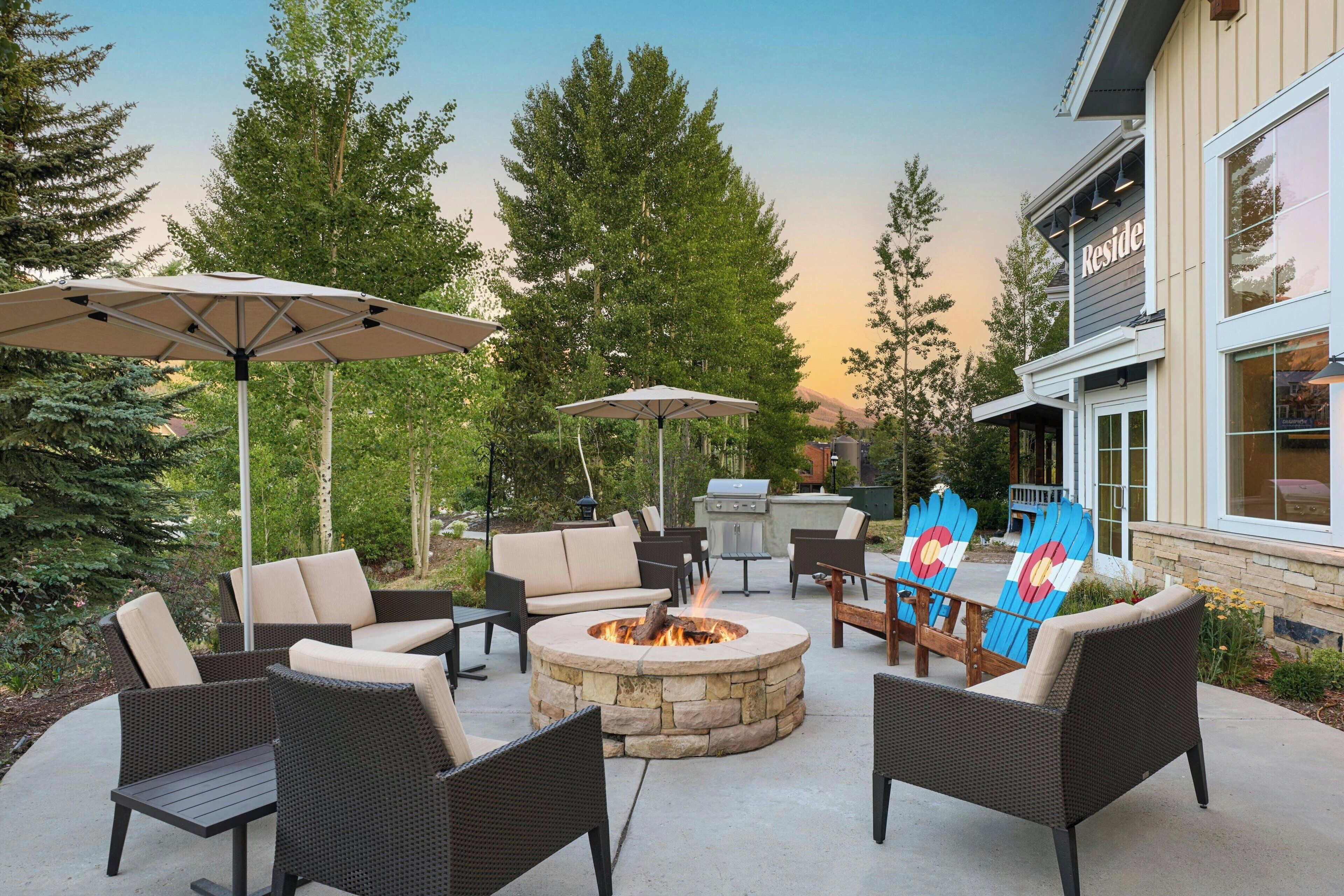 An outdoor patio area with wicker furniture, stone fire pit, and umbrellas.