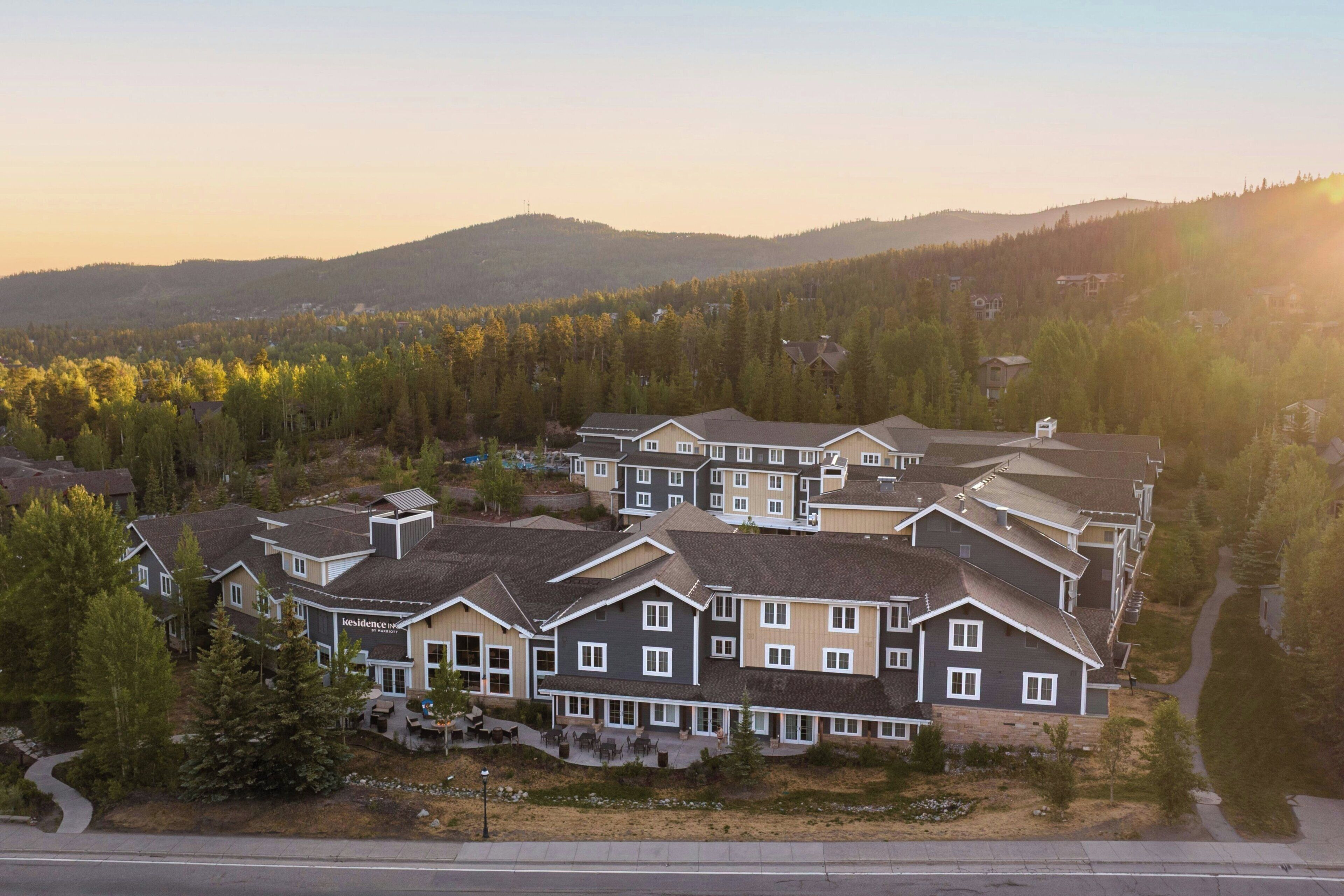 A residential complex with multiple two-story houses, a paved driveway, and a surrounding forested area.