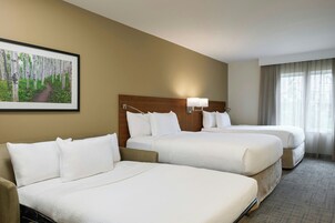 Habitación de hotel con dos camas, cabecero, lámpara de pared y ventana con cortinas.