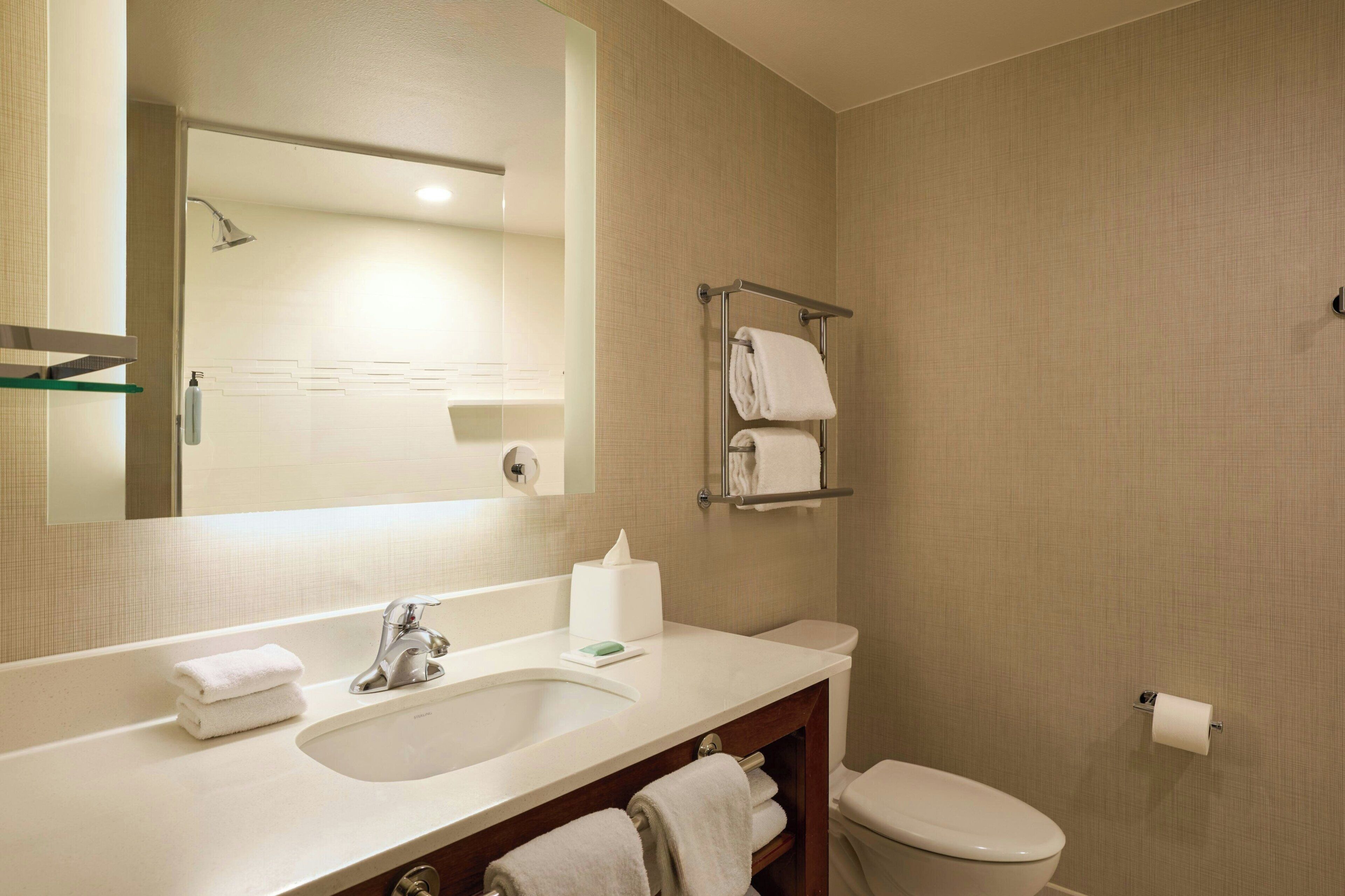 Une salle de bain équipée d’un lavabo, d’un miroir, d’un porte-serviettes, de toilettes et d’un distributeur d’essuie-tout.