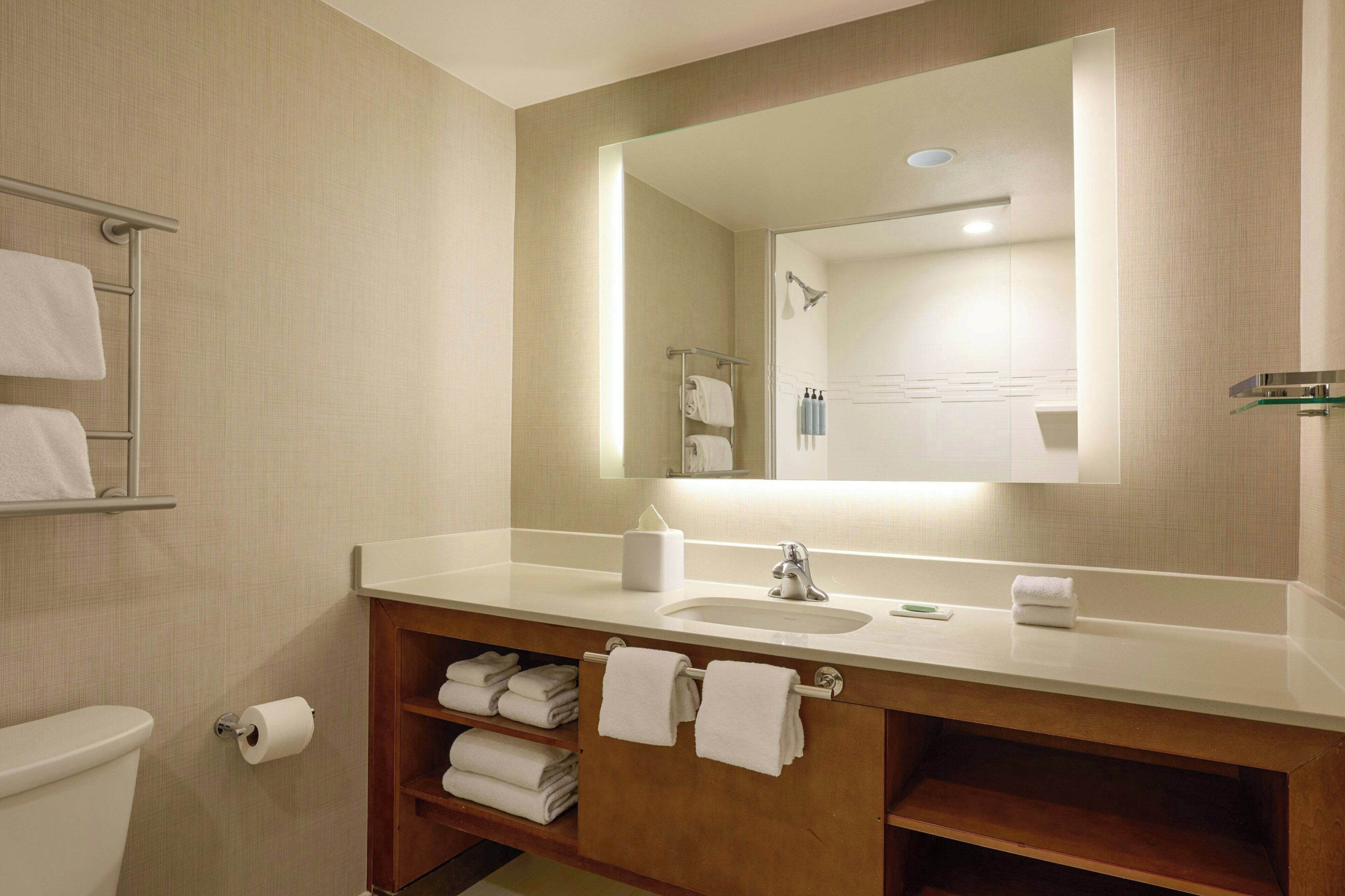 A hotel bathroom with a wooden vanity, a sink, a mirror, and a towel rack.