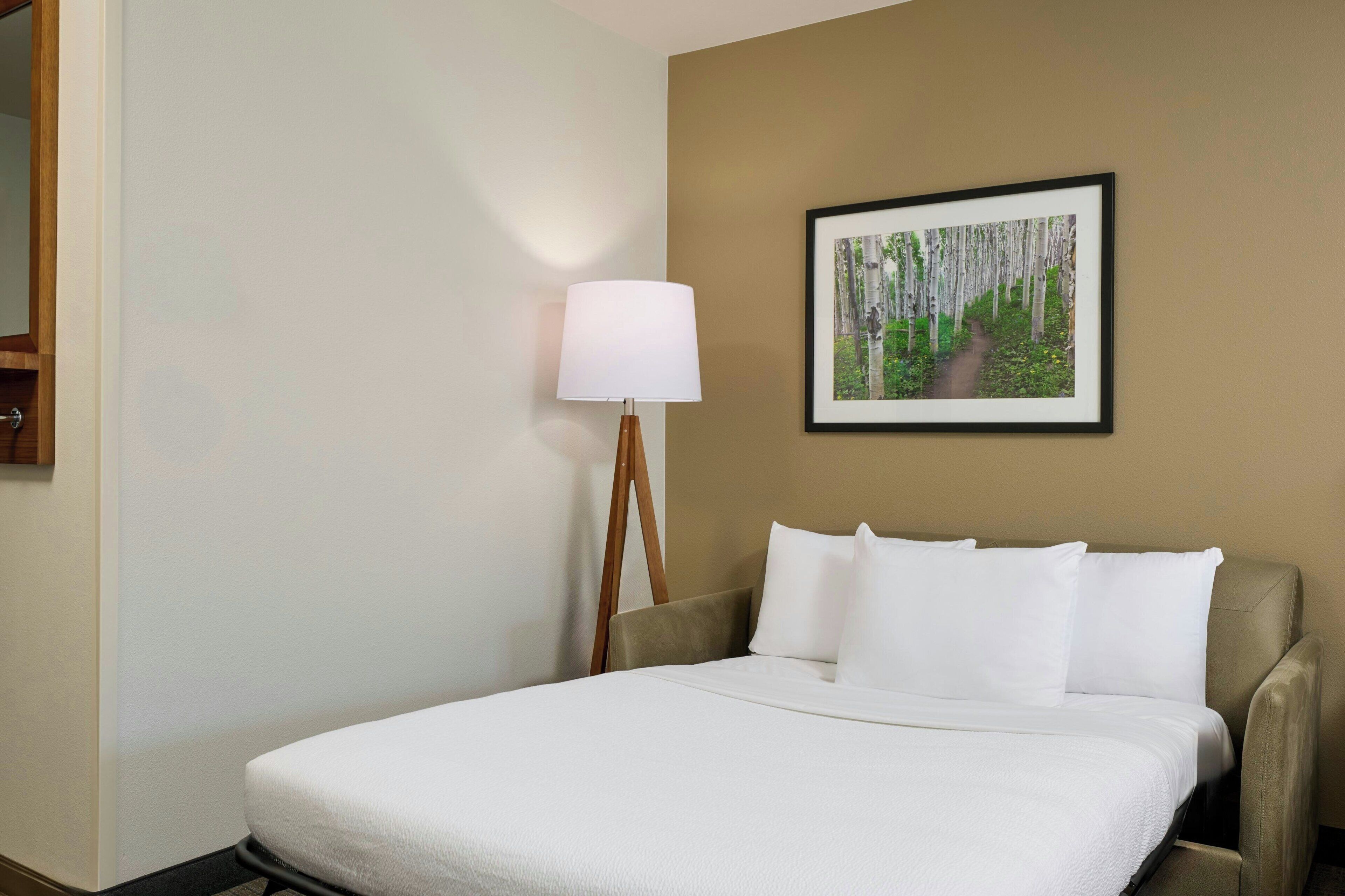 A hotel room with a bed, a lamp, and a framed picture on the wall.