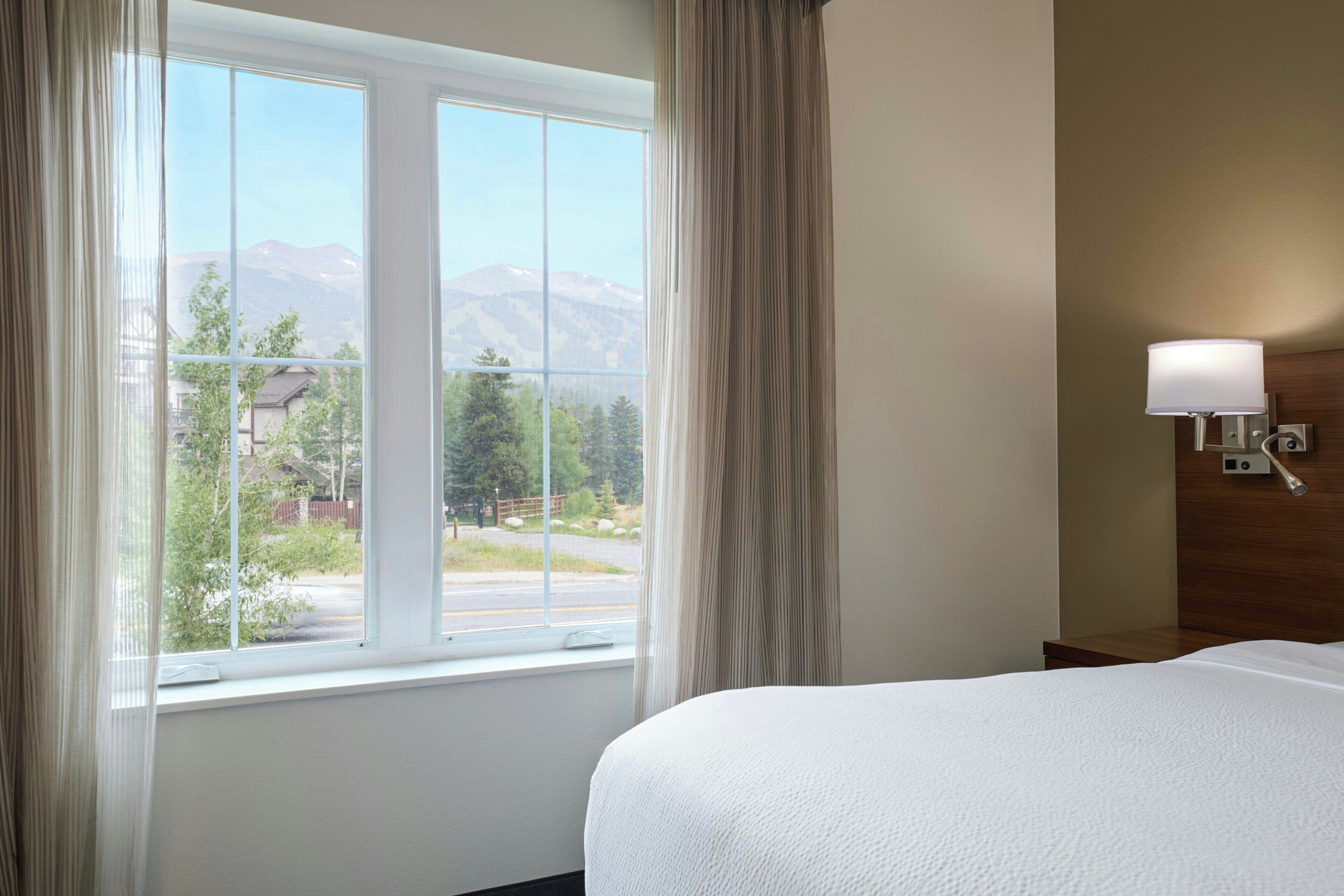 Habitación de hotel con un ventanal grande, una cama y una lámpara de pared.