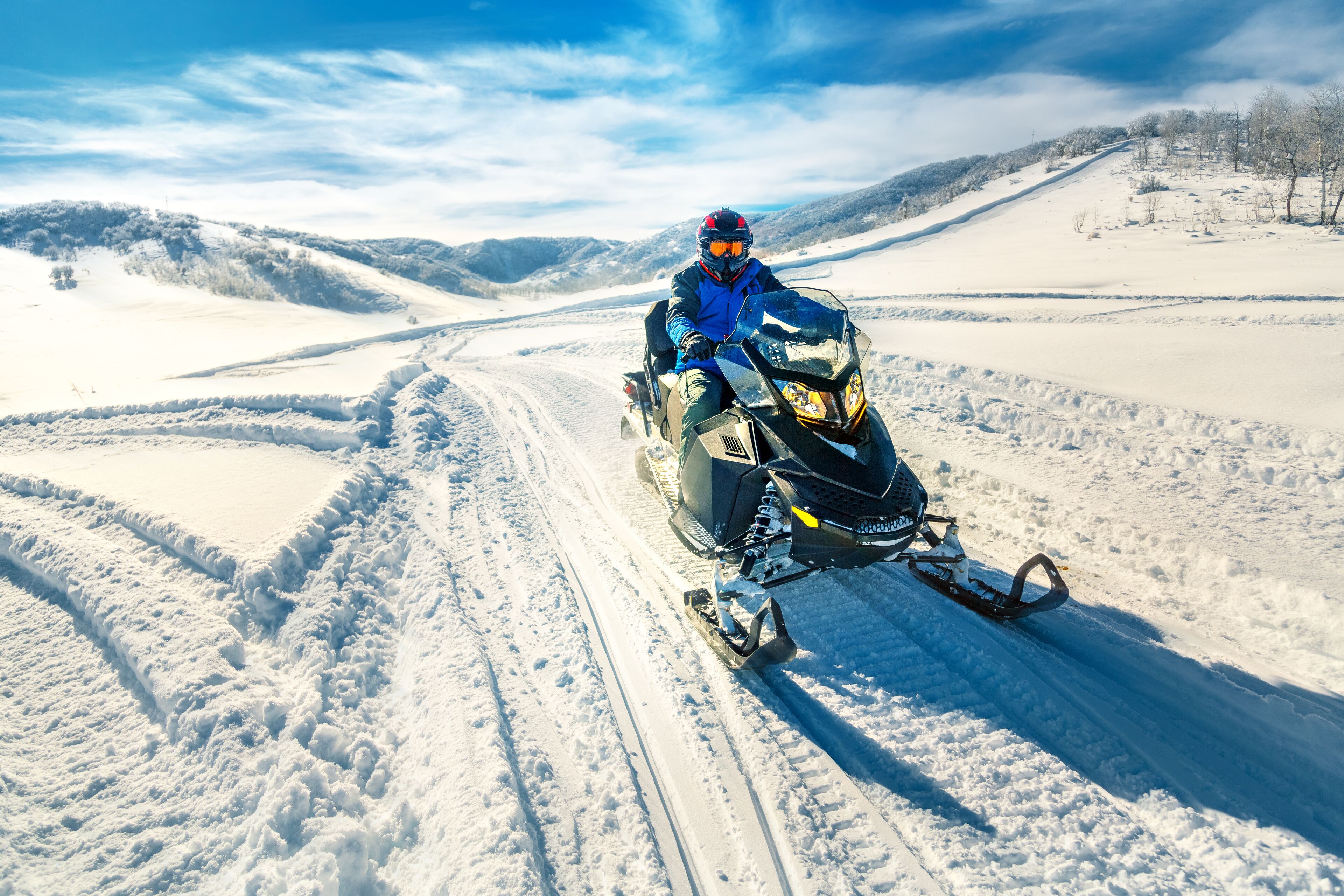 A snowmobile on a snowy path with a hilly landscape in the background.