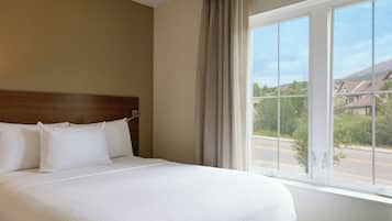 A hotel room with a large bed, a wooden headboard, and a window with a view of houses and greenery.