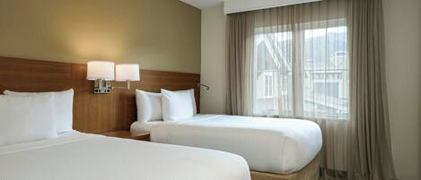 A hotel room with two beds, a wooden headboard, a nightstand, and a window with curtains.
