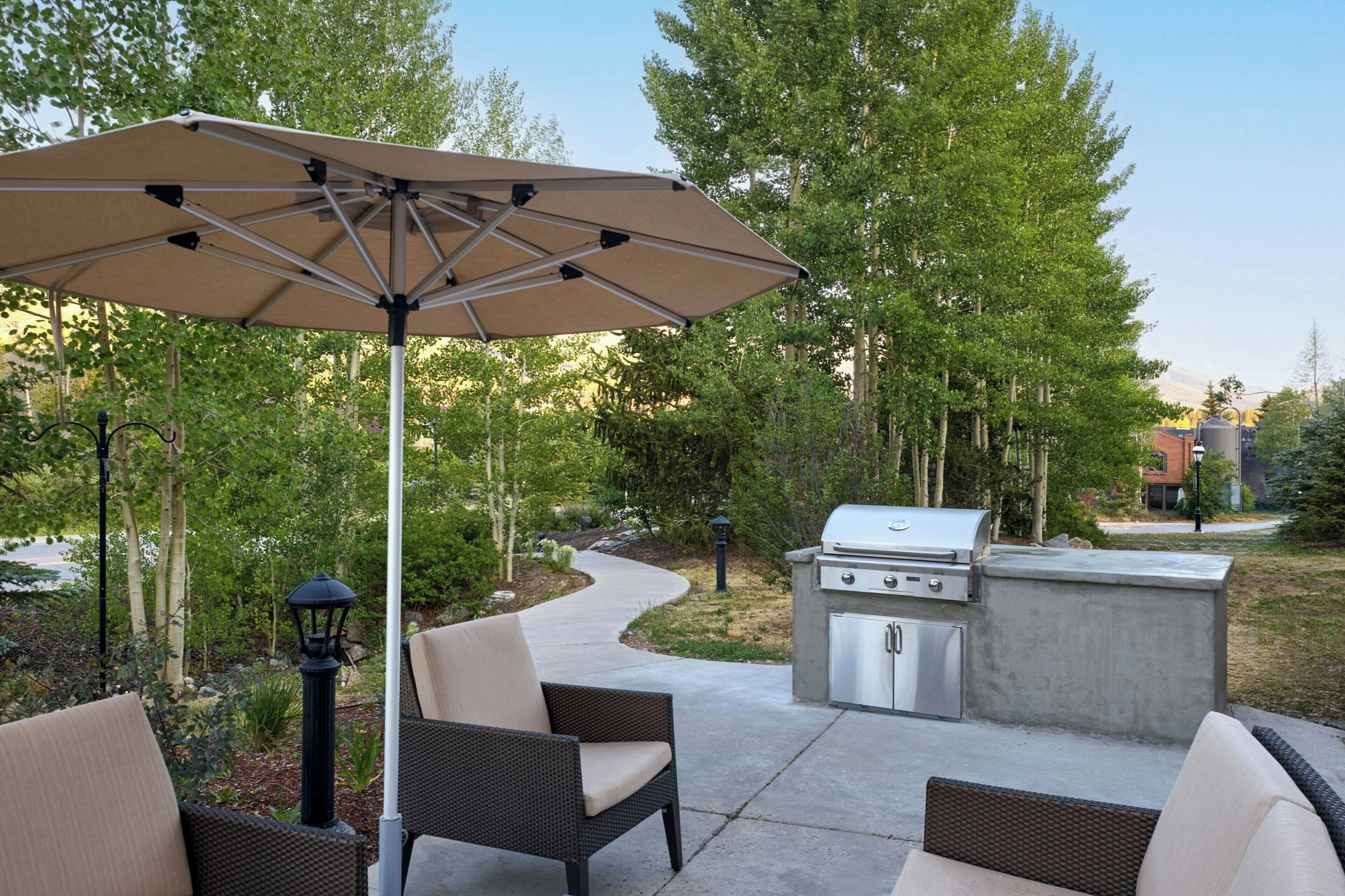 An outdoor patio with a grill, seating, and an umbrella.
