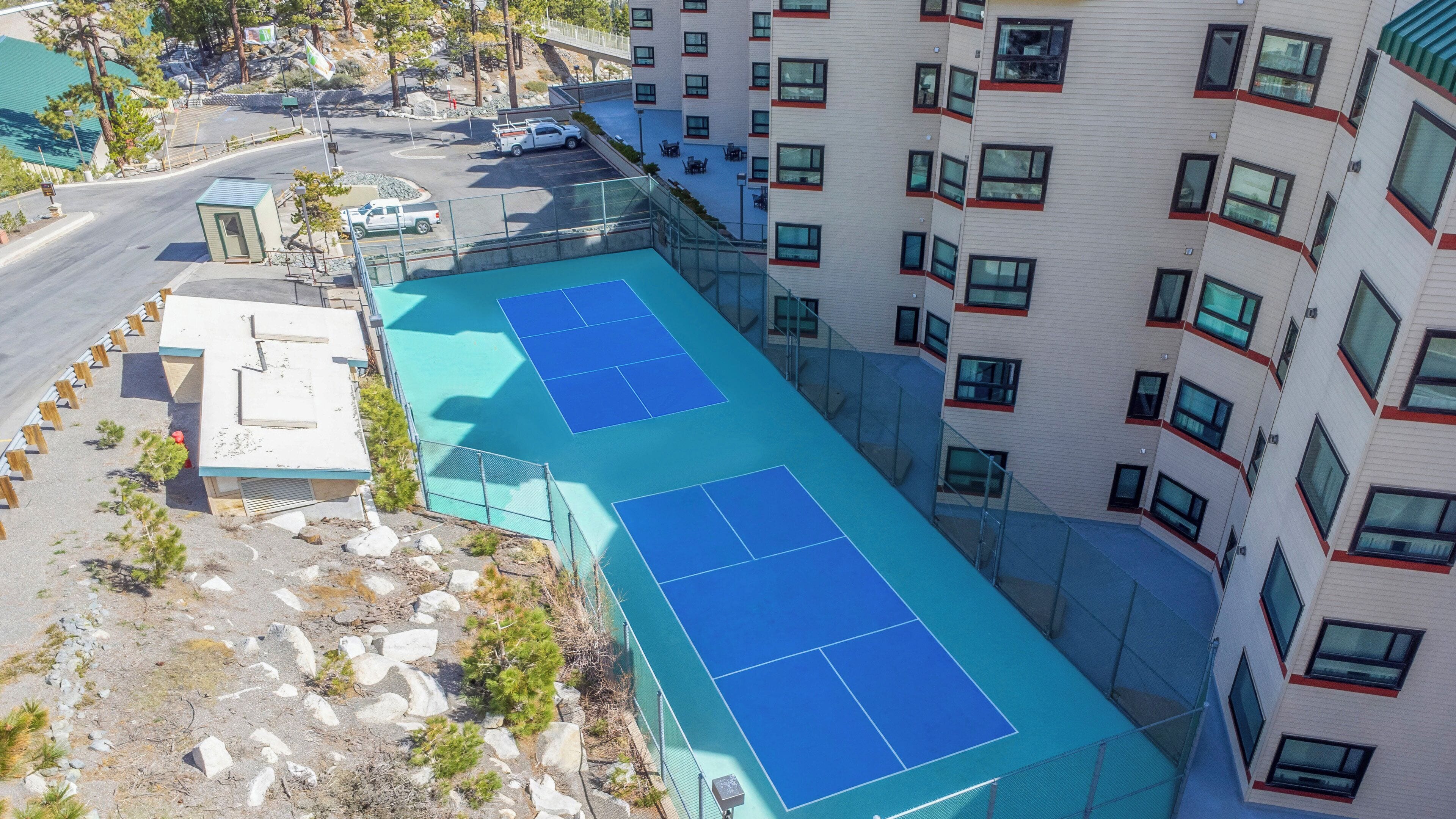 Ein mehrstöckiges Gebäude mit Dachterrasse und Tennisplatz sowie einem Parkplatz.