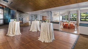 A spacious hall with a stone fireplace, multiple round tables with white tablecloths, and a view of the outdoors through large windows. - Holiday Inn Club Vacations Tahoe Ridge Resort by IHG (Stateline)