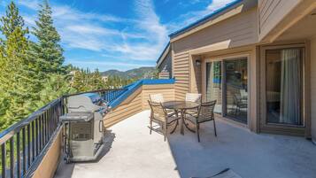 A balcony with a grill, chairs, and a view of trees and mountains.