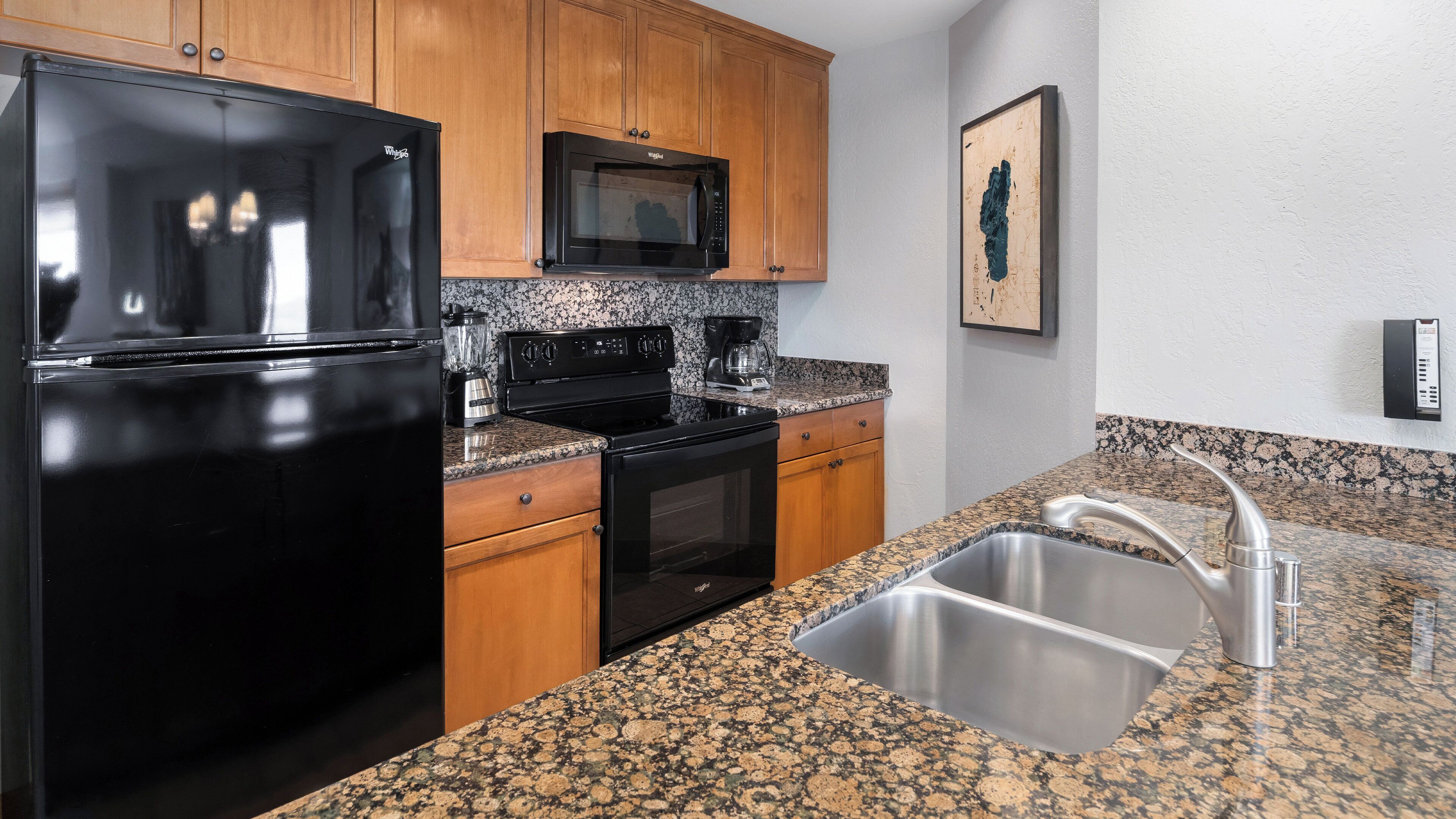 A kitchen with a refrigerator, microwave, stove, oven, sink, and granite countertop.