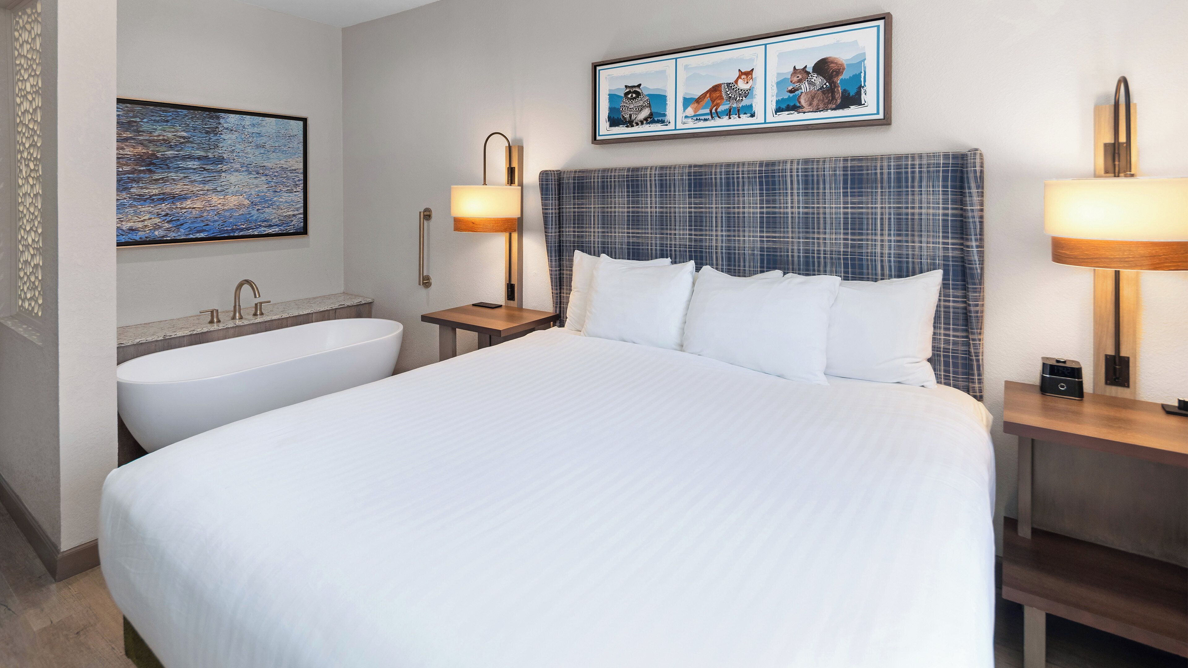 A hotel room with a large bed, a bathtub, a nightstand with a lamp, and a framed picture on the wall.