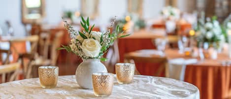 A round table with a white tablecloth, a vase with white flowers, and three textured candle holders.