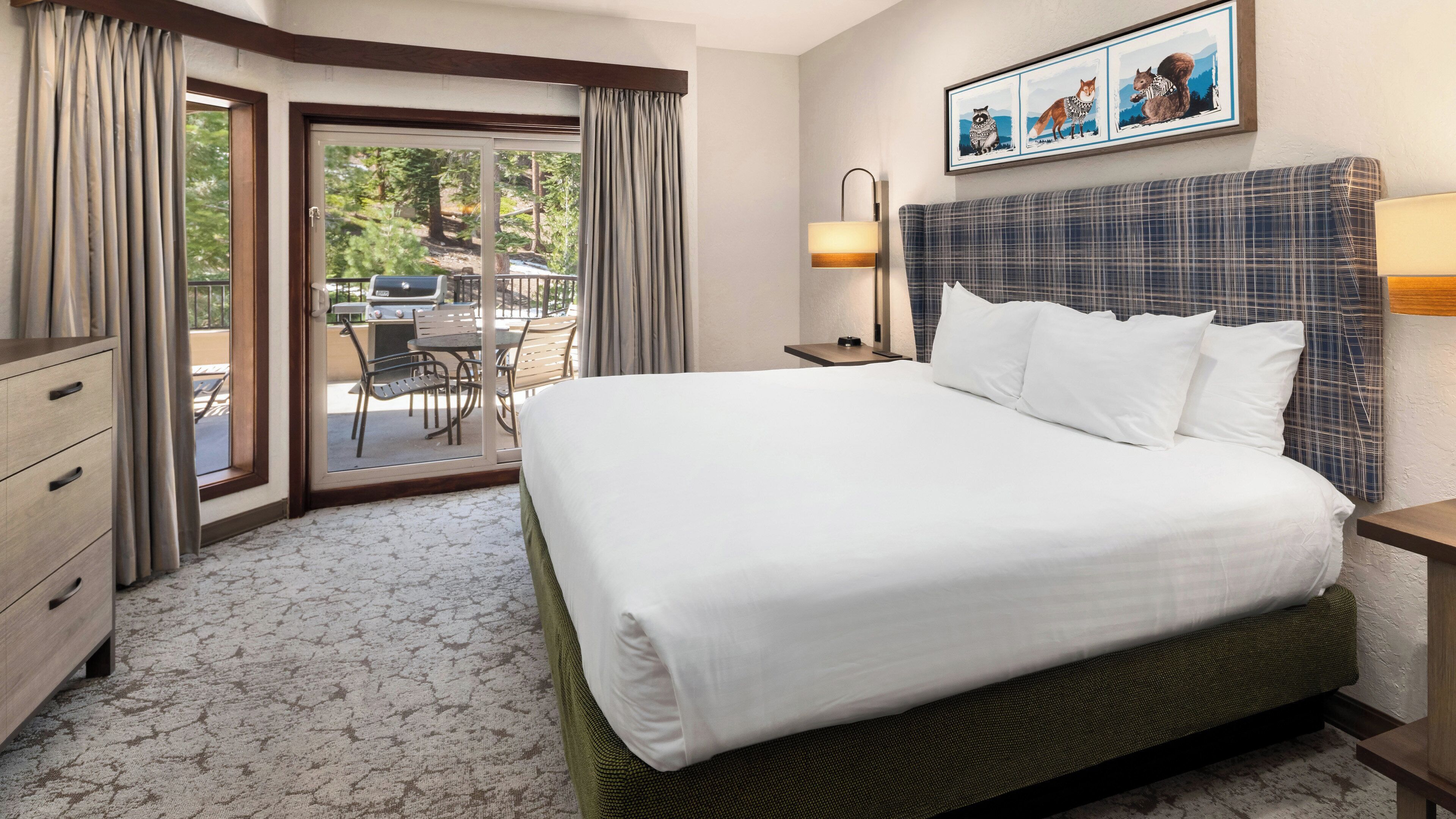 A hotel room with a large bed, a desk, a chair, a window with curtains, and a picture on the wall.