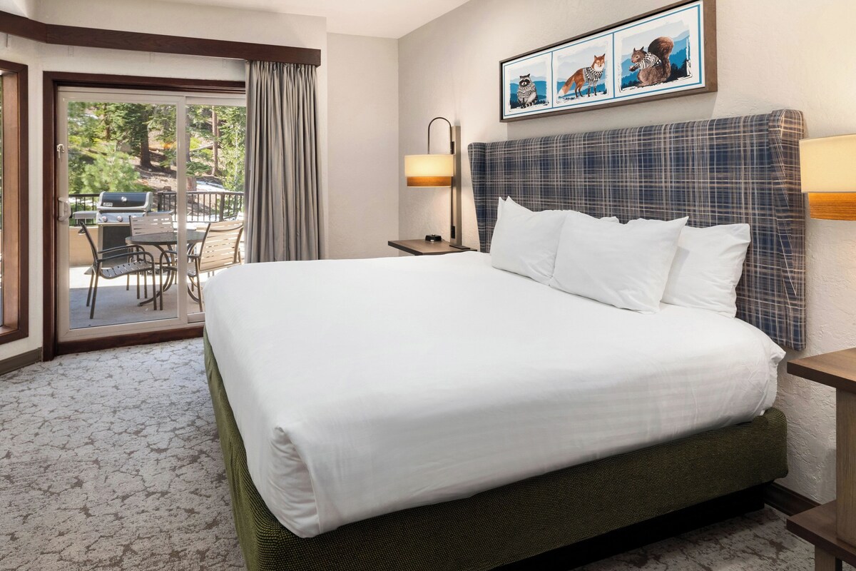 Een hotelkamer met een groot bed, een bureau, een stoel, een raam met gordijnen en een schilderij aan de muur.