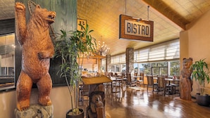 Interior de restaurante com decoração em madeira, um letreiro com a palavra 'BISTRO' e uma escultura de urso.